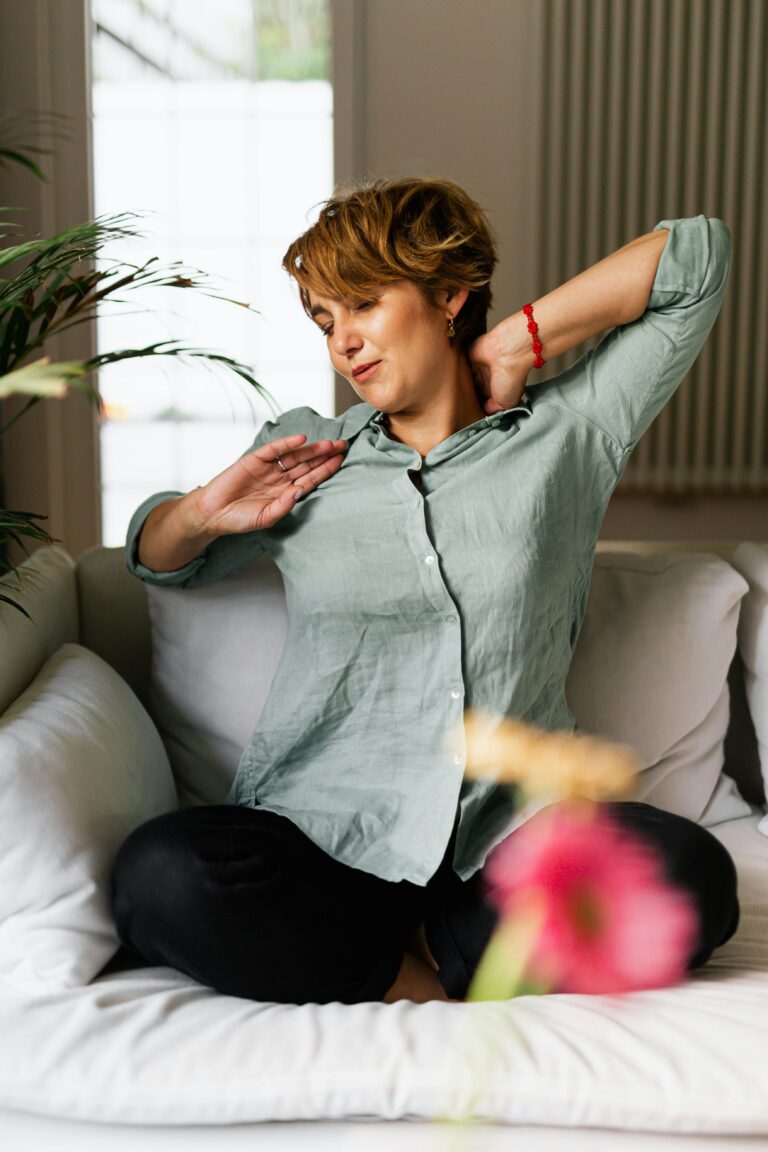 A woman in a green shirt stretches comfortably on a sofa indoors.